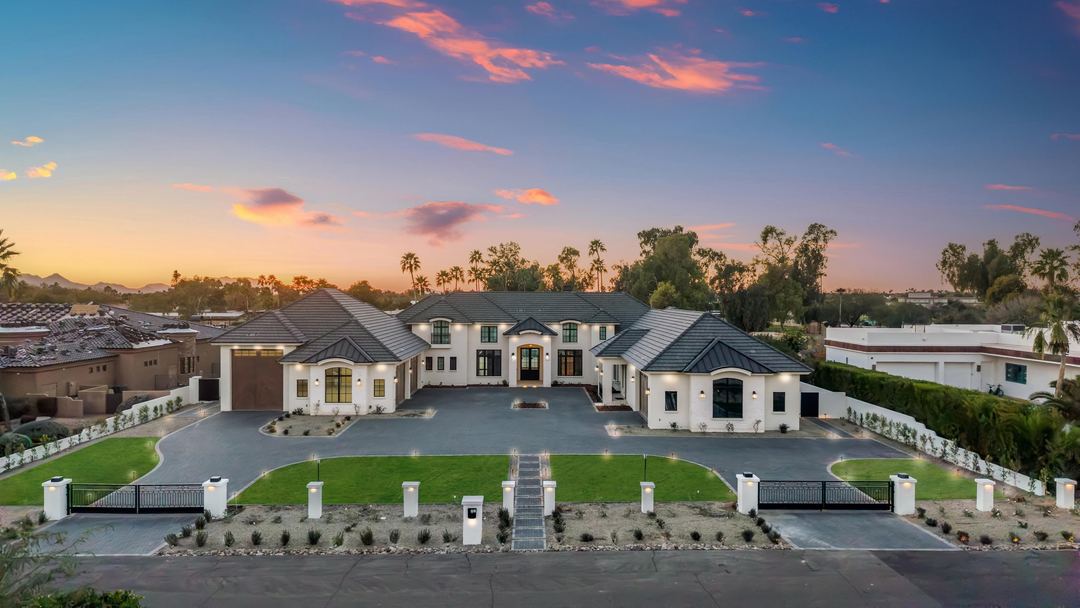 Twilight aerial of a gated estate with a long lawn and a lit motor court
