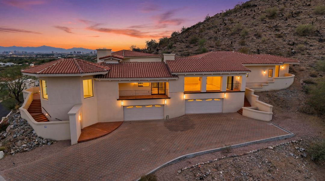 Hillside home at dusk with every window lit, its motor court and stairways cut into the mountain
