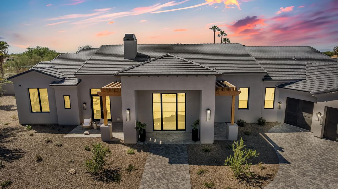 Front of a modern home at dusk with a cedar pergola and lit windows