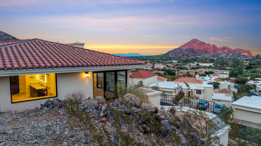 Camelback Mountain glowing at sunset beyond a tile roof and a lit window