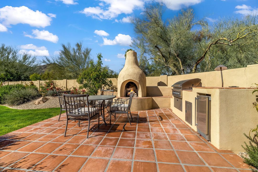 Outdoor kitchen with a kiva fireplace and a dining set on a tile patio