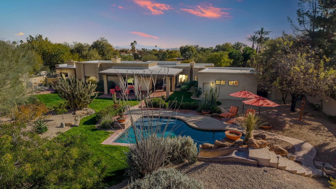 Twilight aerial of a backyard with a free-form pool, red umbrellas and a lawn