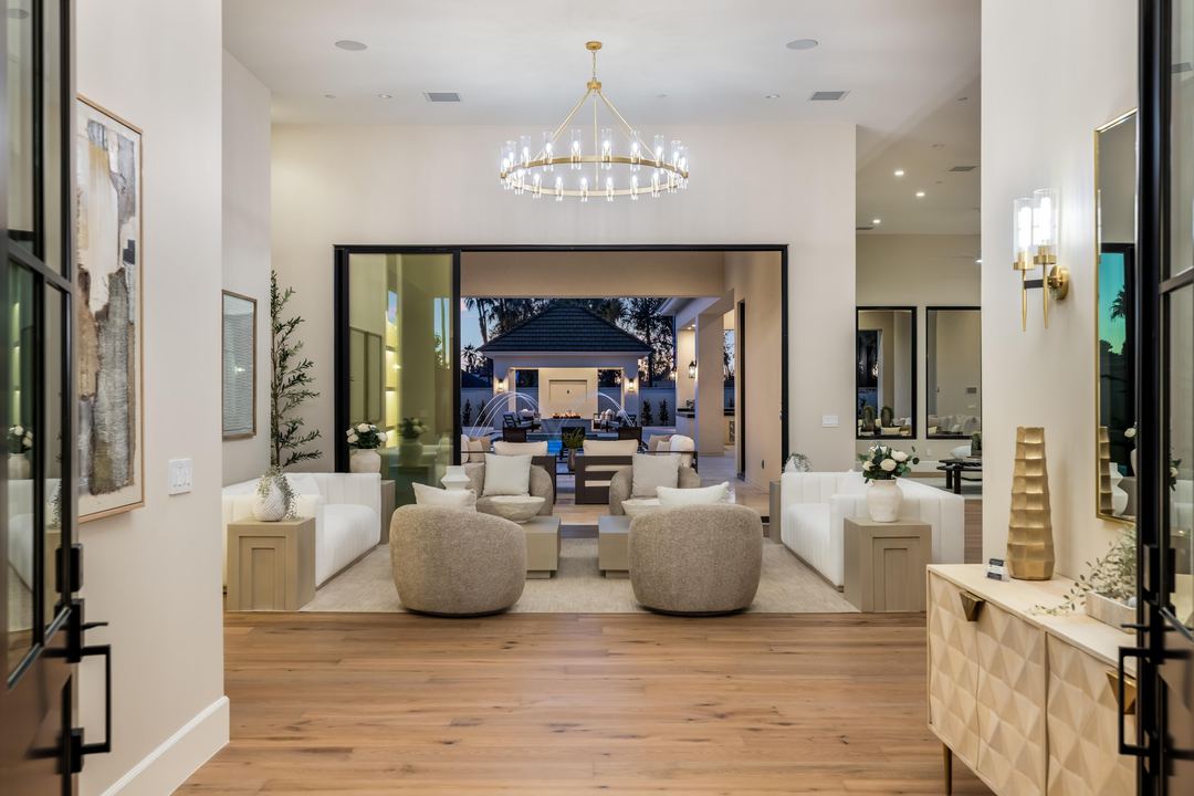 Living room with a ring chandelier, looking through glass doors to the pool cabana