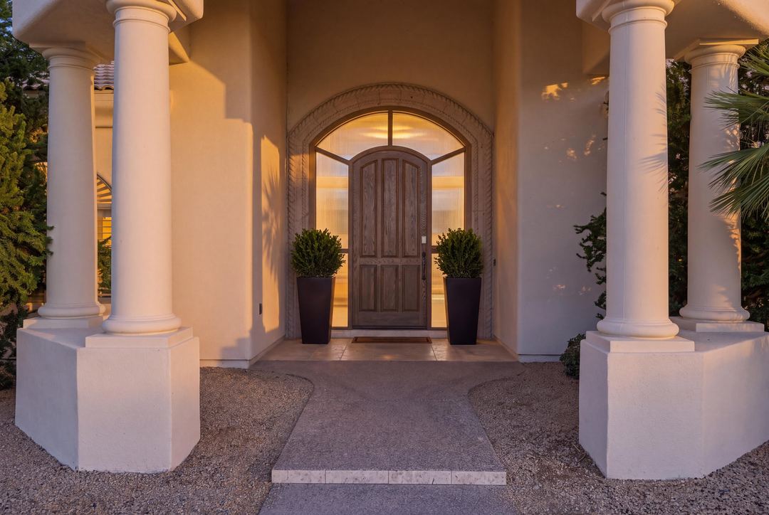Columned entry with an arched wood door, lit at twilight