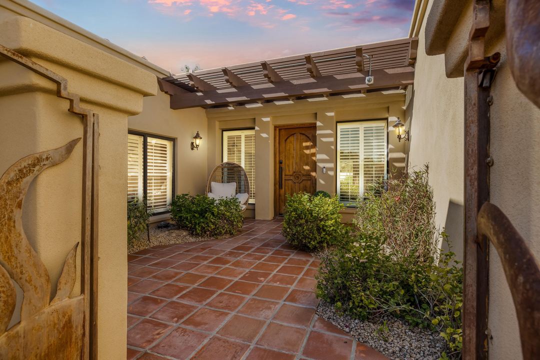 Tiled entry courtyard at dusk with a carved wood door and a pergola