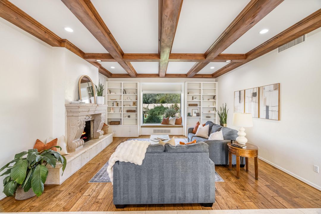 Living room with a beamed ceiling, a carved stone fireplace and built-in shelves
