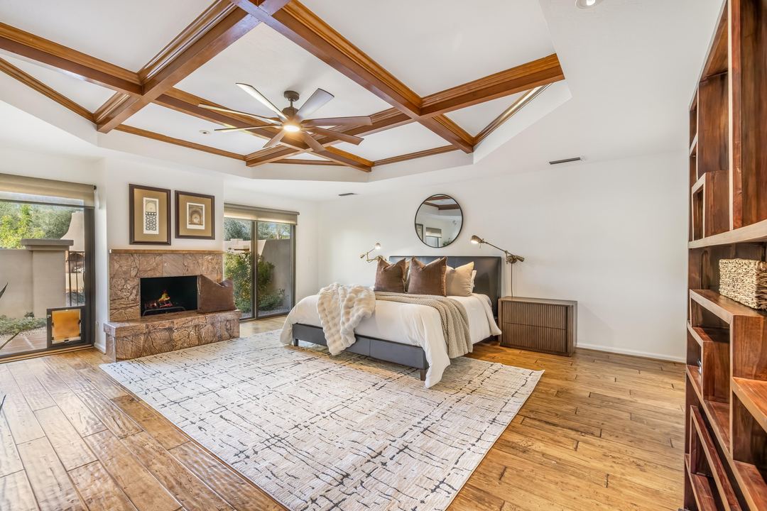 Primary suite with a coffered wood ceiling, a stone fireplace and hardwood floors