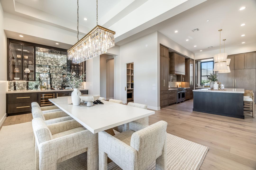 Dining room under a crystal chandelier, open to a mirrored bar