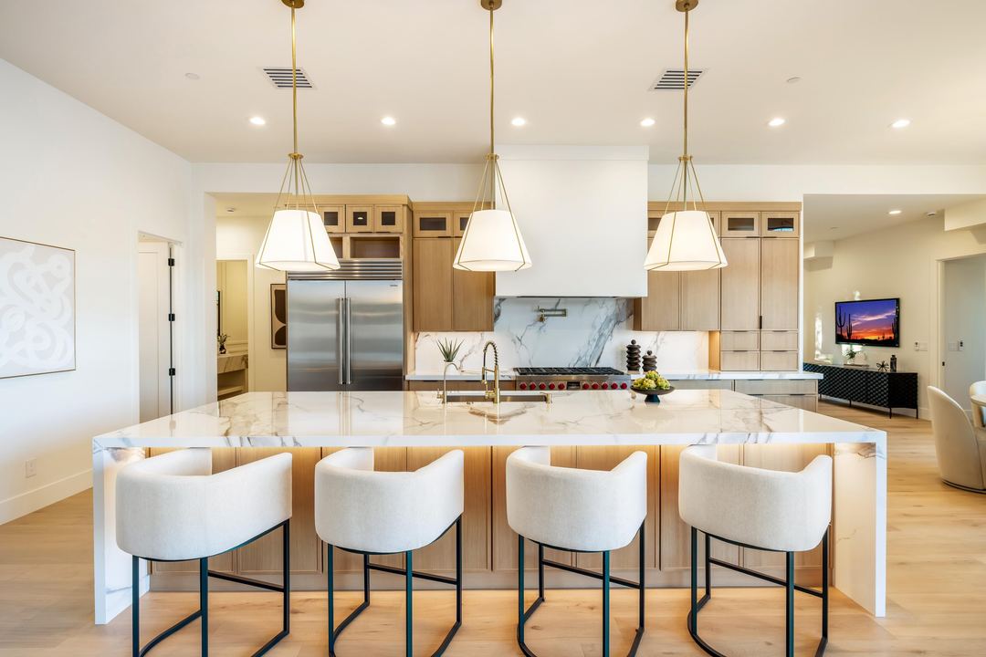 Kitchen with a marble island, four cream stools and brass pendants