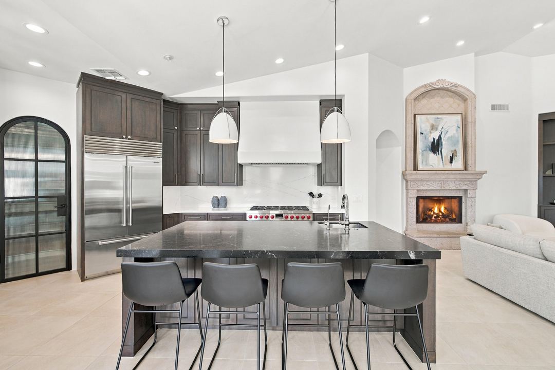 Kitchen with a dark island, a stone fireplace and an arched steel pantry door