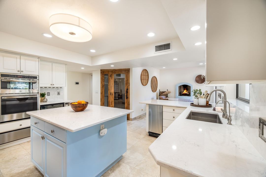 White kitchen with a pale blue island, quartz counters and a kiva fireplace beyond