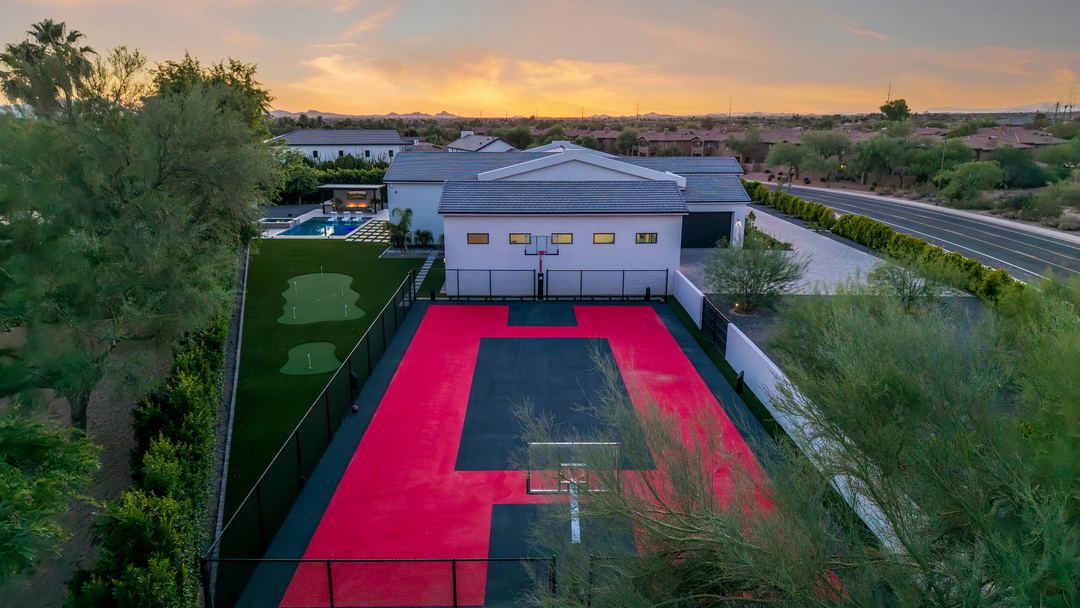 Twilight aerial of a red sport court and pool behind a modern white home