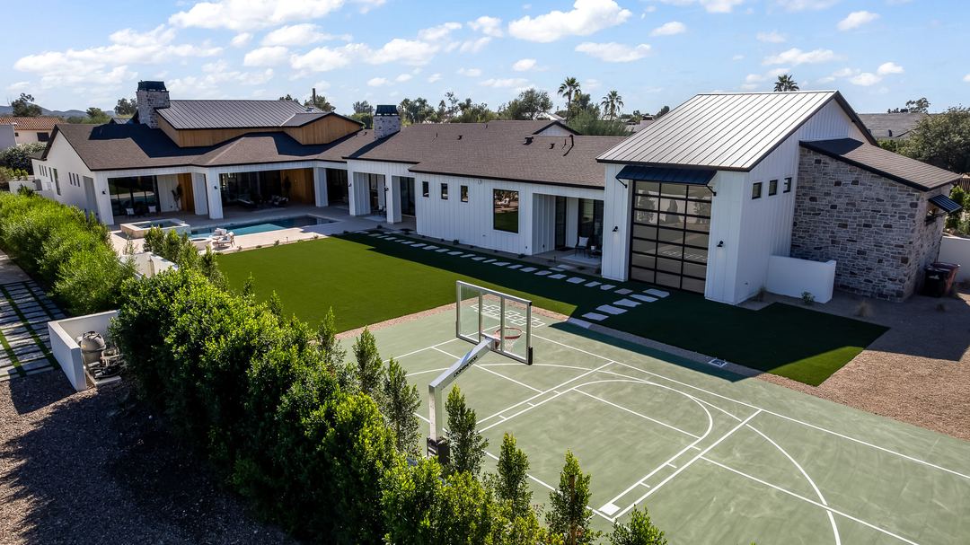 Aerial over the backyard sport court, pool and lawn of a modern farmhouse
