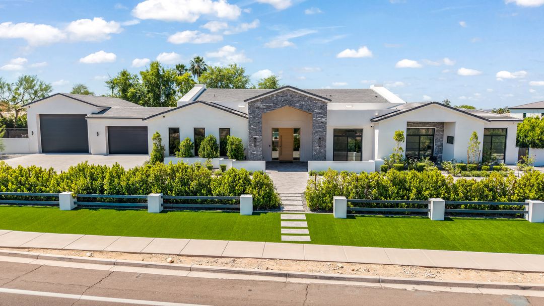 Daytime aerial of a modern farmhouse with a paver motor court and clipped hedges
