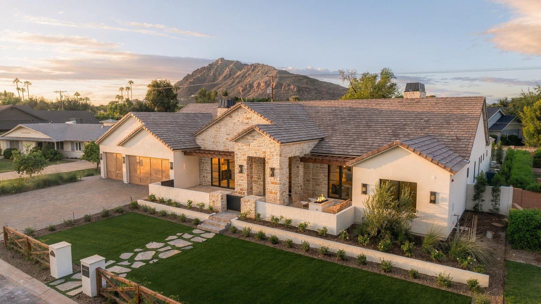 Twilight aerial of a stone and stucco home on a corner lot, with Camelback Mountain behind it