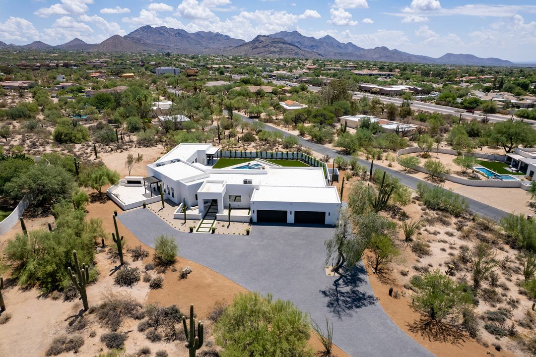 Wide aerial of a white modern home on a desert lot with mountains behind