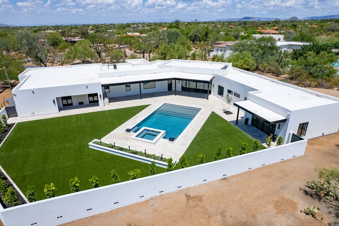 Aerial of a white desert modern home with a pool and lawn, surrounded by desert