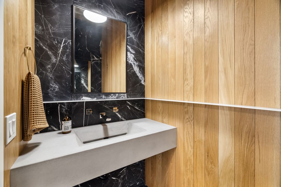 Restroom with black marble, oak paneling and a concrete sink