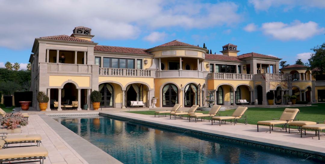 A Mediterranean estate with a long pool and lawn under a blue sky, a frame from its listing film