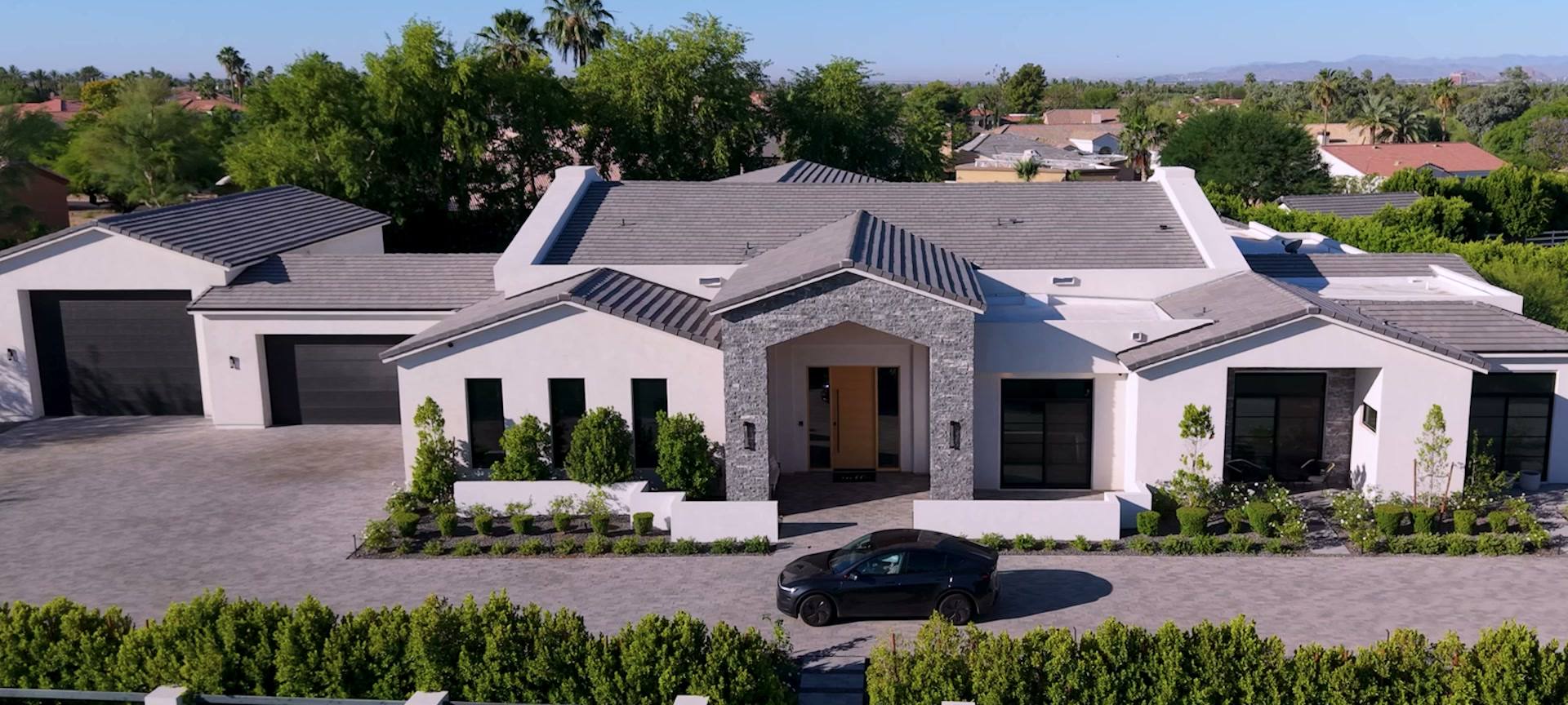Aerial of a white modern farmhouse with a stone entry and a black car in the drive, a frame from its listing film