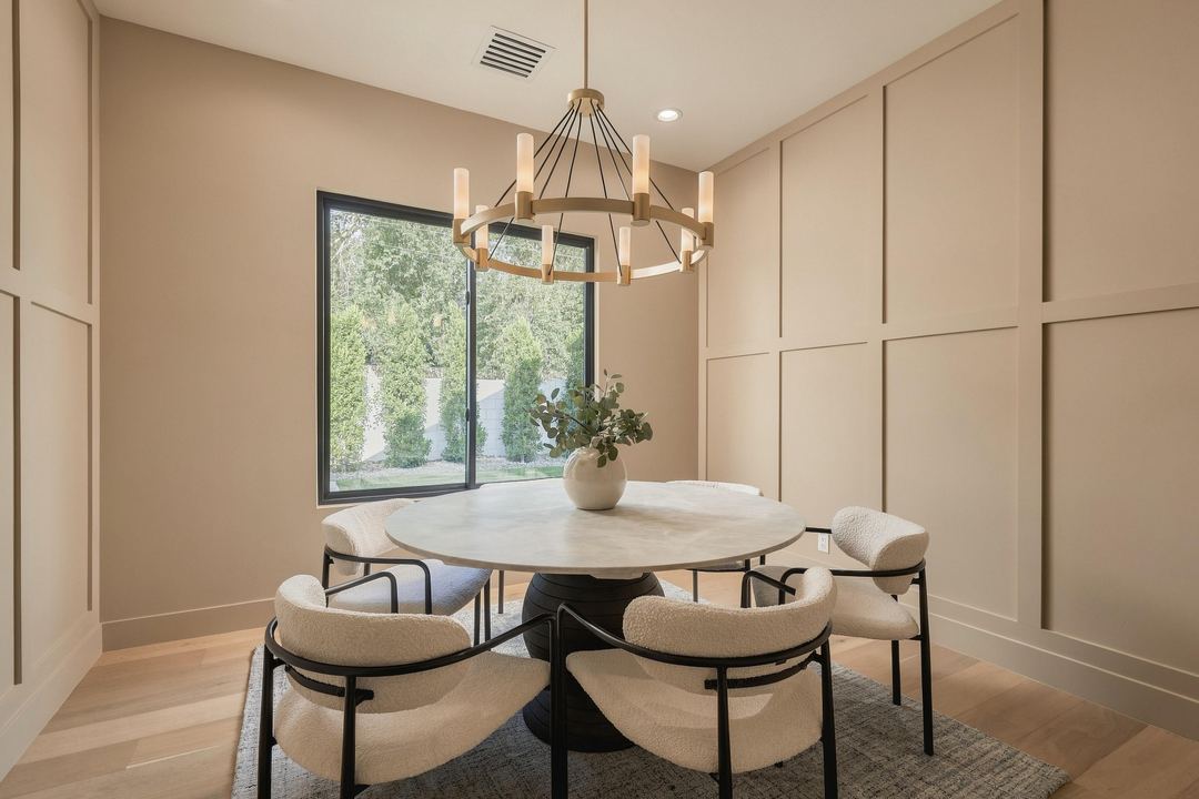 Dining room with a round stone table, cream boucle chairs, a ring chandelier and board-and-batten walls