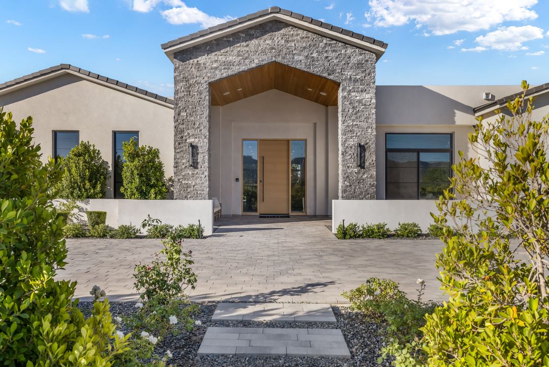 Stone-clad entry with a tall oak door, framed by desert plantings, in daylight