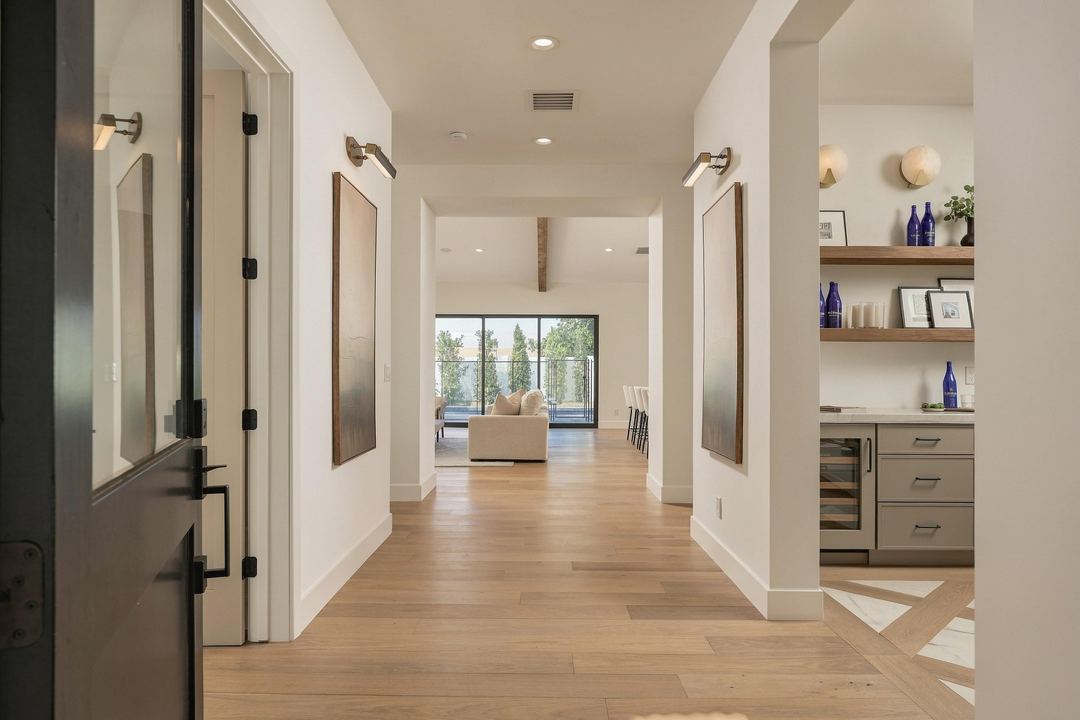 Looking through the open front door down a wide oak-floored hall to the great room and the pool, with a bar and wine fridge off to the right