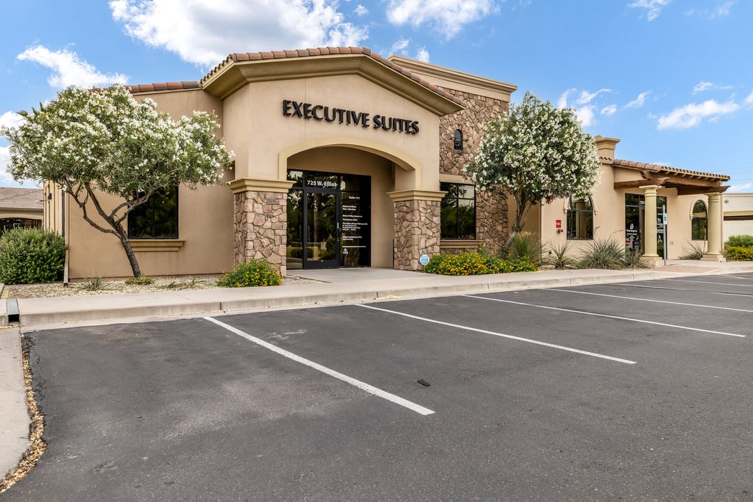 Executive Suites office building with a tiled roof and parking lot under a blue sky