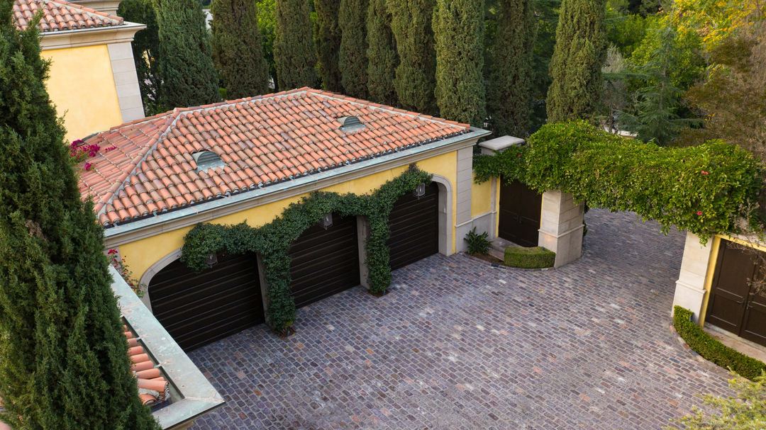 Aerial of a tiled roof, cypress trees and a cobbled motor court