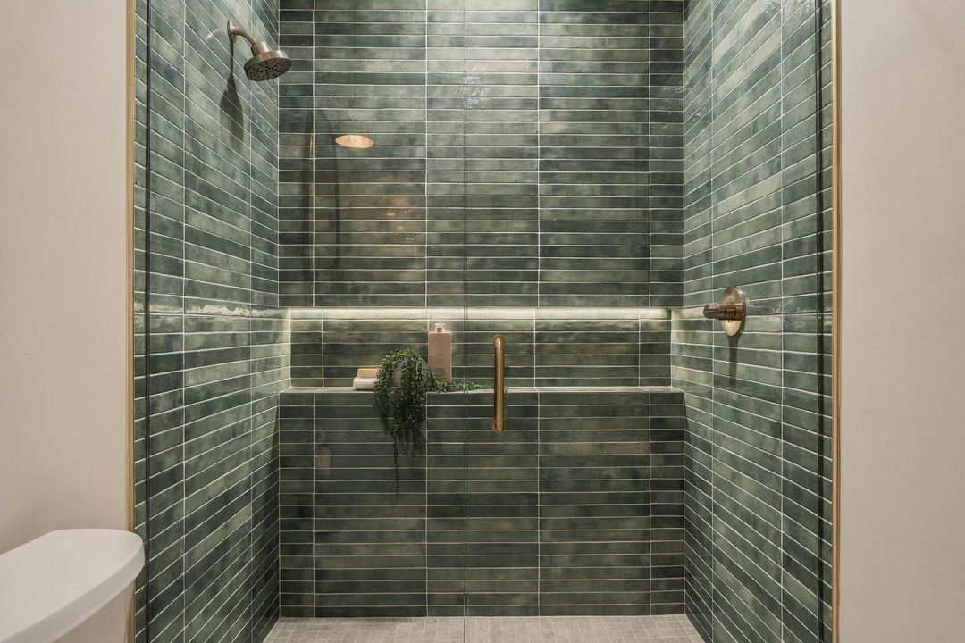 Walk-in shower tiled in glossy green, with a lit niche and brass fixtures