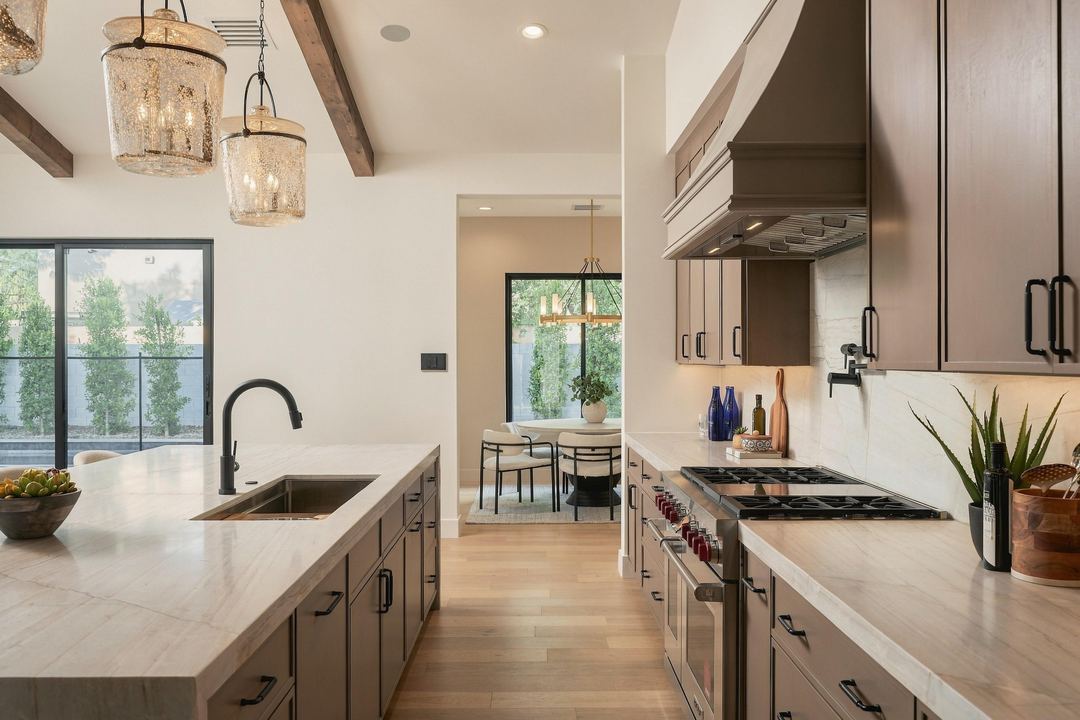 Quartz island with a black faucet, a gas range under a wood hood, and the dining nook through the doorway beyond