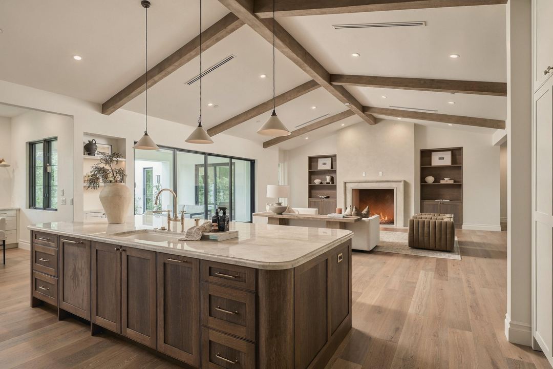 Kitchen and great room under a beamed ceiling, with a walnut island and the fireplace beyond