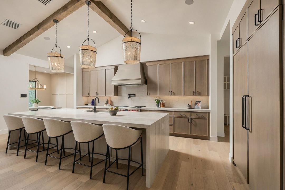 Kitchen with a long quartz waterfall island, five cream stools and three mercury-glass pendants under a beamed ceiling