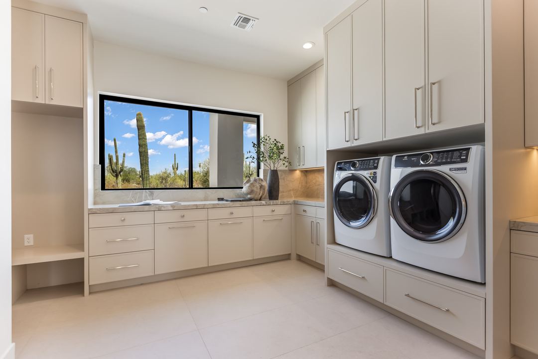 Laundry room with white cabinets and a window onto the desert
