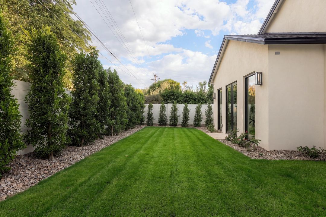 Long back lawn edged with hedges and gravel, running past the glass doors of the house