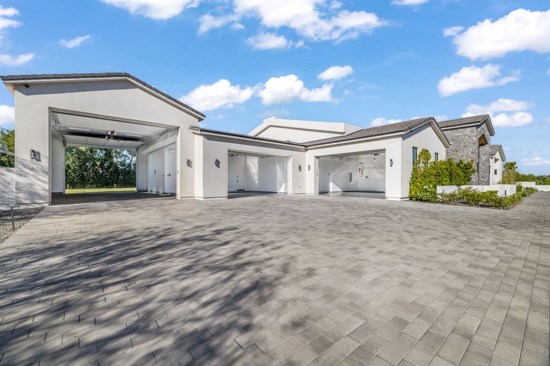 Paver motor court and garages of a modern white home under a blue sky