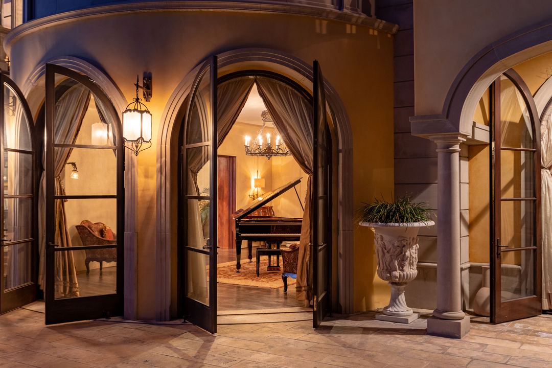 Arched doors open to a lit room with a grand piano