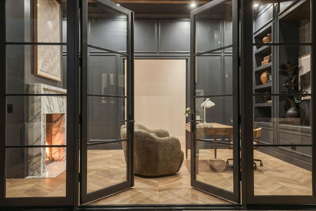 The office seen through black steel glass doors, with the fire lit