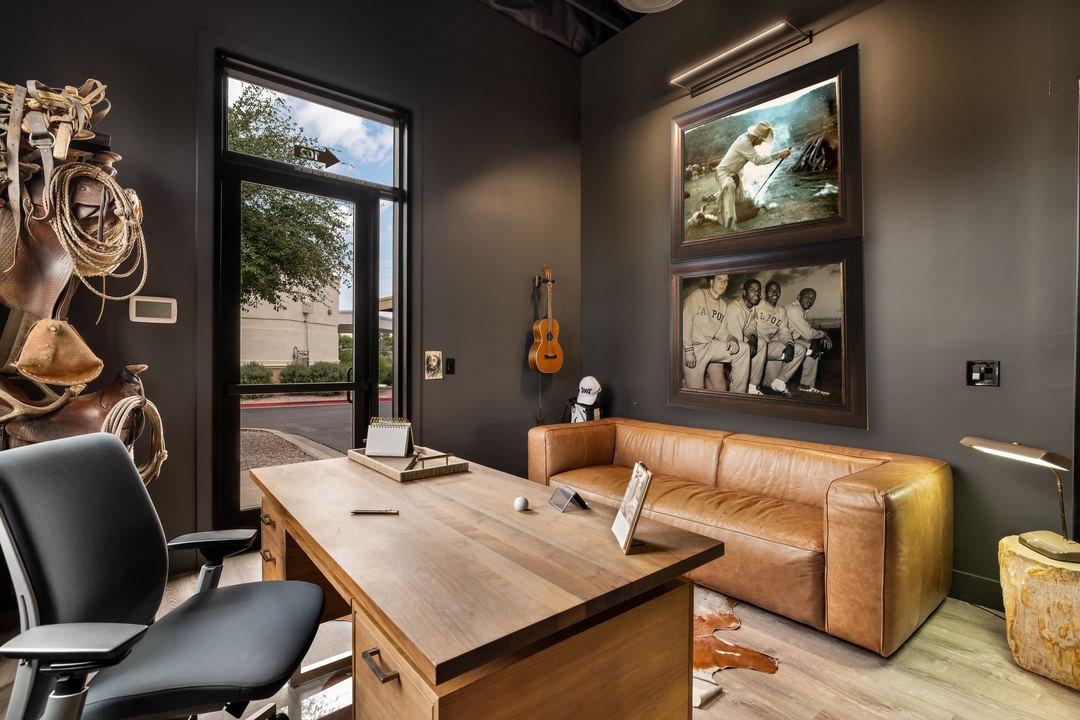 Office with black walls, a wood desk and tan leather chairs