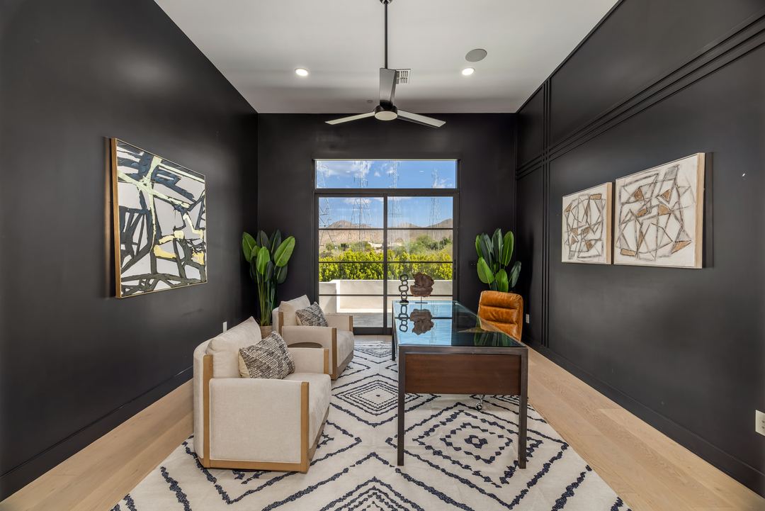 Home office with black walls, a glass desk and a mountain view through a tall window