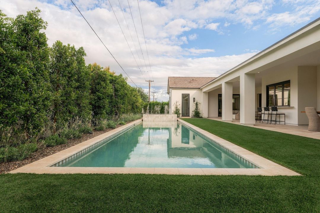 Lap pool and lawn between the house and a wall of hedges, in daylight