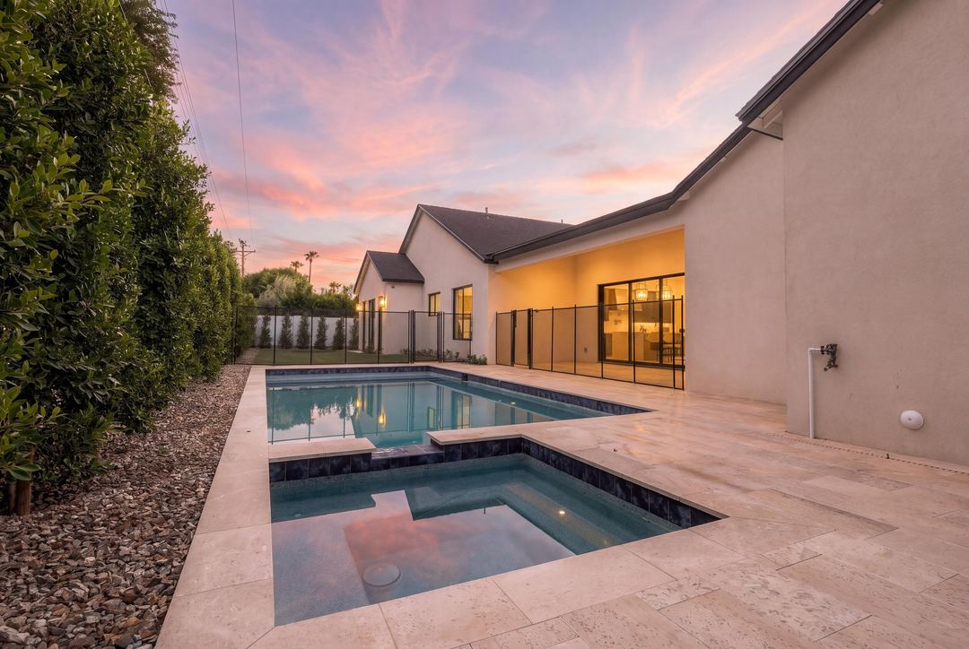 Pool and raised spa at twilight on a travertine deck, the house lit behind them under a pink sky