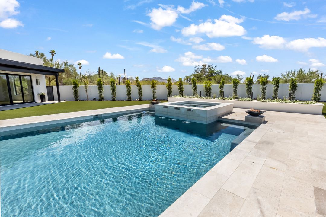 Backyard pool and spa with a white wall and desert trees behind