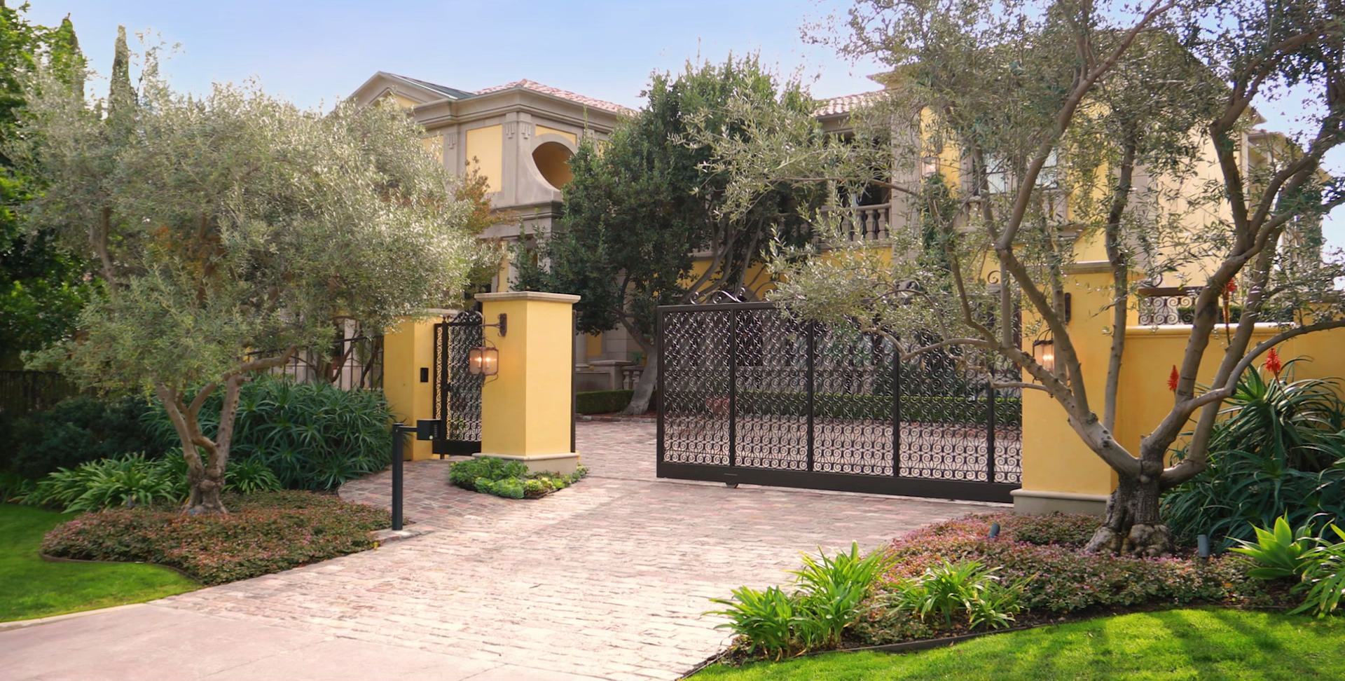 The iron gates and motor court of a Mediterranean estate in Beverly Hills, the opening frame of its listing film
