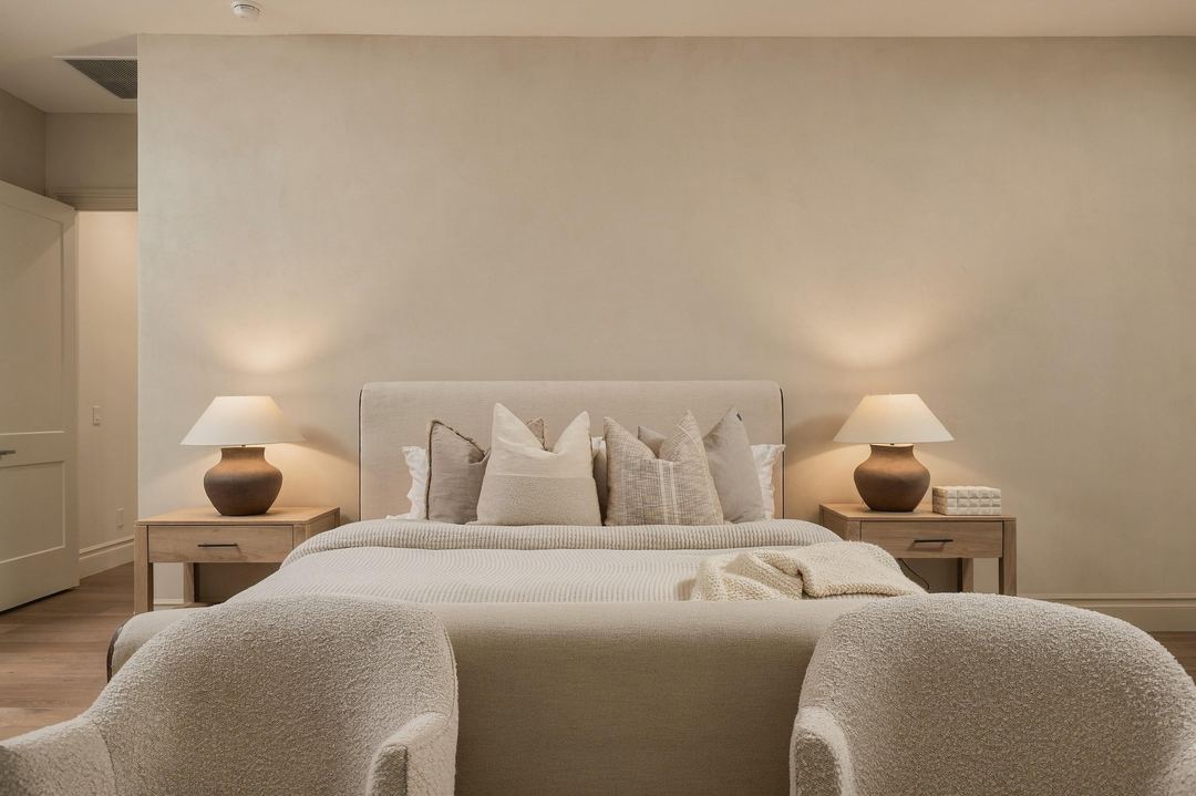 Primary bedroom with an upholstered bed, two boucle lounge chairs and a glass door to the yard