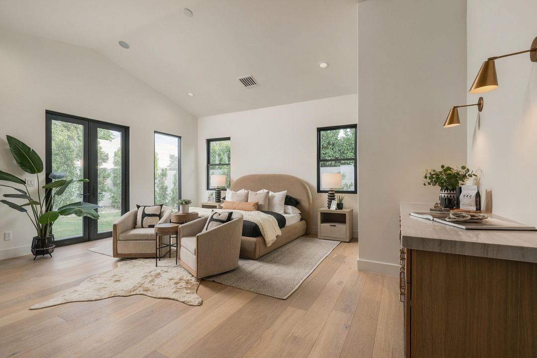 Primary bedroom with a vaulted ceiling, French doors to the yard, a tan upholstered bed and two armchairs on a cowhide rug