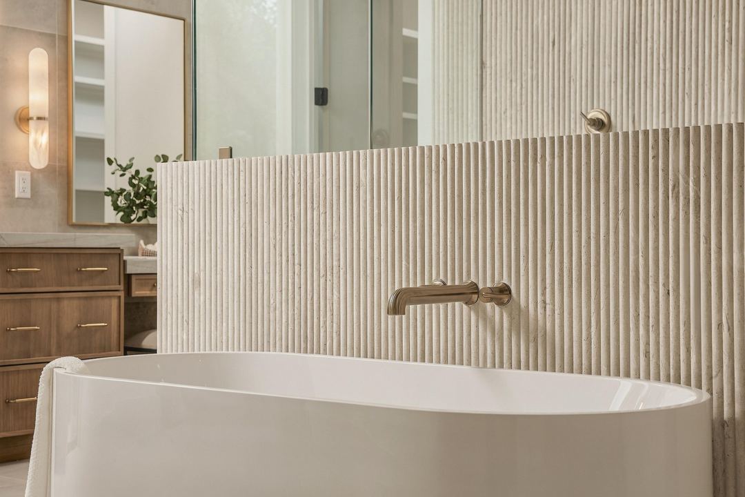 Freestanding white tub with a brass wall-mounted filler against a fluted stone half wall