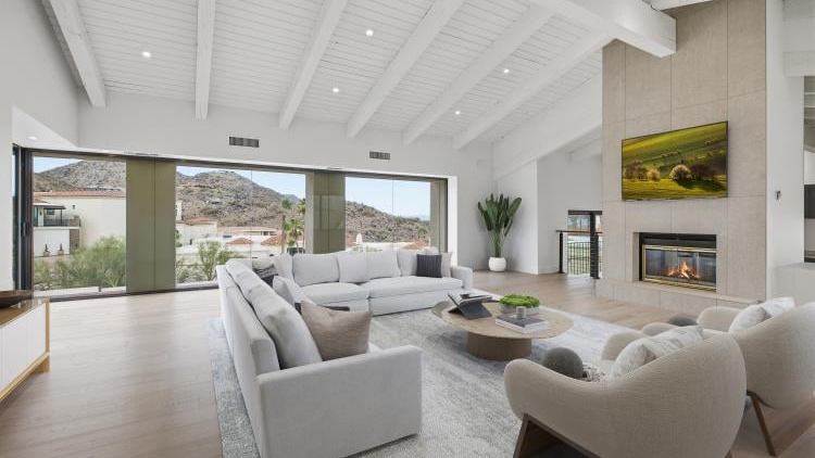 Great room with a beamed ceiling and fireplace, empty and then virtually staged: staged