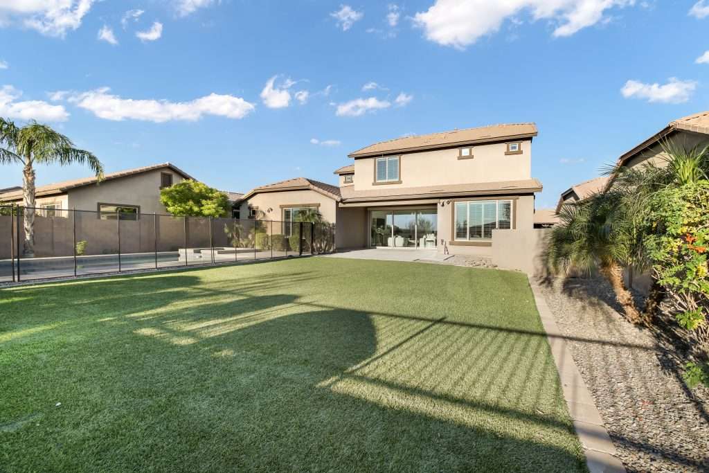 Real estate photography in Scottsdale AZ of a two-story home exterior with backyard lawn and pool fence